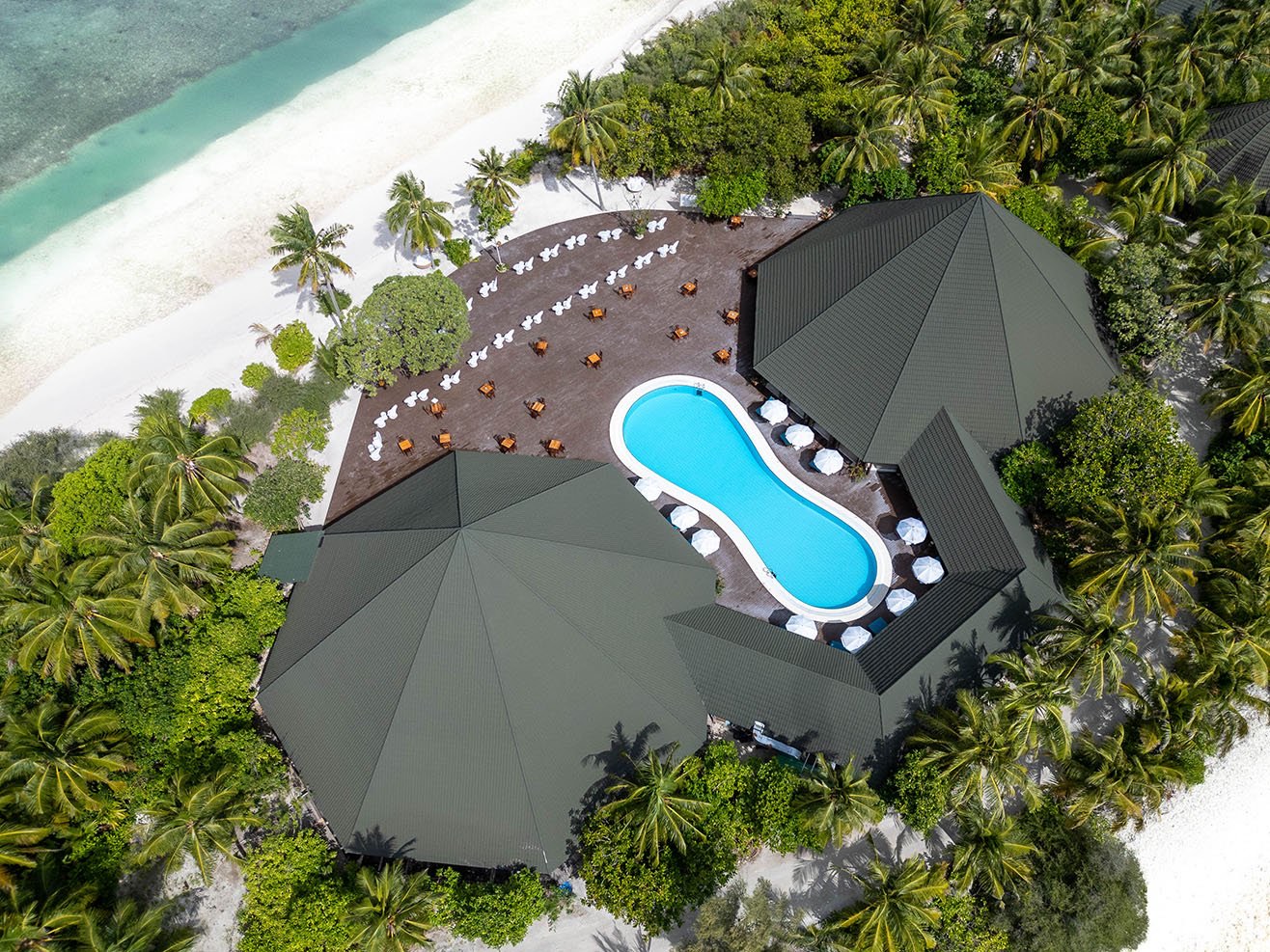 Aerial view over the resort's pool deck and thatched roofs, with the beach and lagoon on one side.