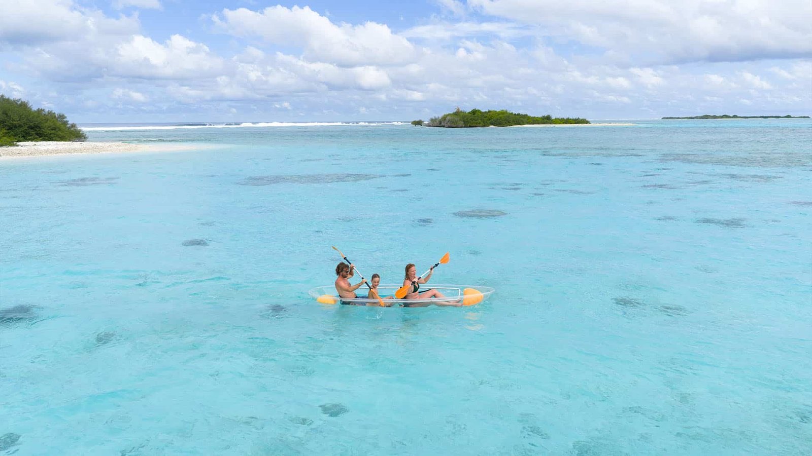 A clear-bottomed glass kayak floating on shallow, bright turquoise water.